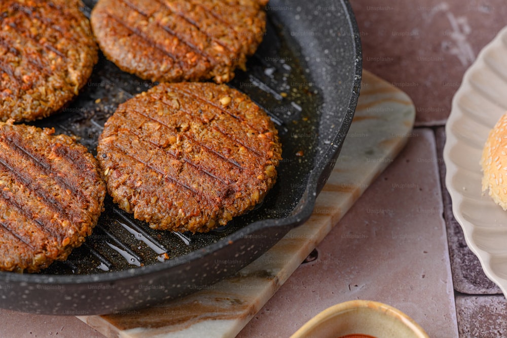 hamburger patties cooking in a frying pan on a table