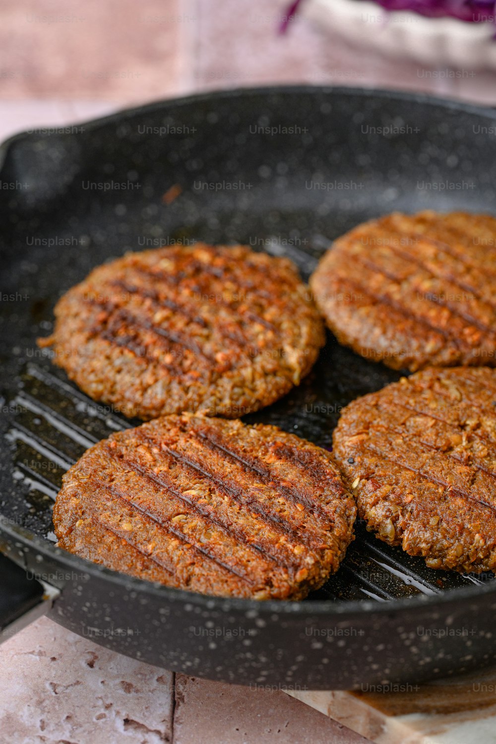 four hamburger patties cooking in a frying pan