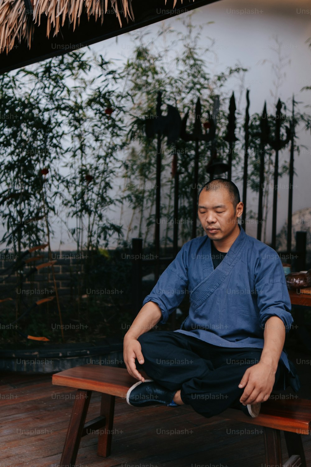 um homem sentado em um banco em frente a uma cabana de bambu