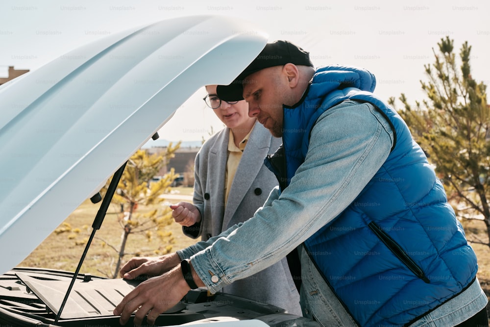 a man and a woman looking at a laptop under a car hood