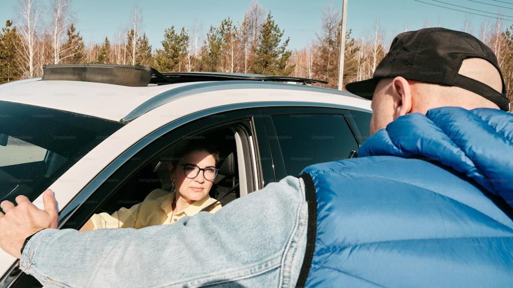 a man in a blue puffy jacket talking to a woman in a white car