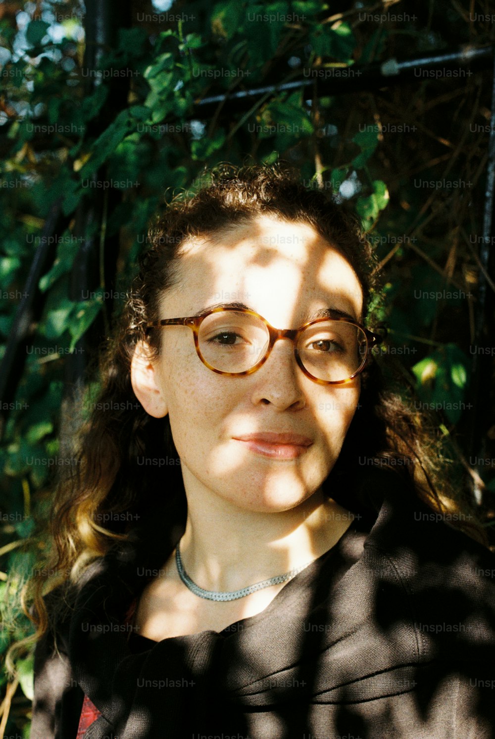 a woman wearing glasses standing in front of a tree