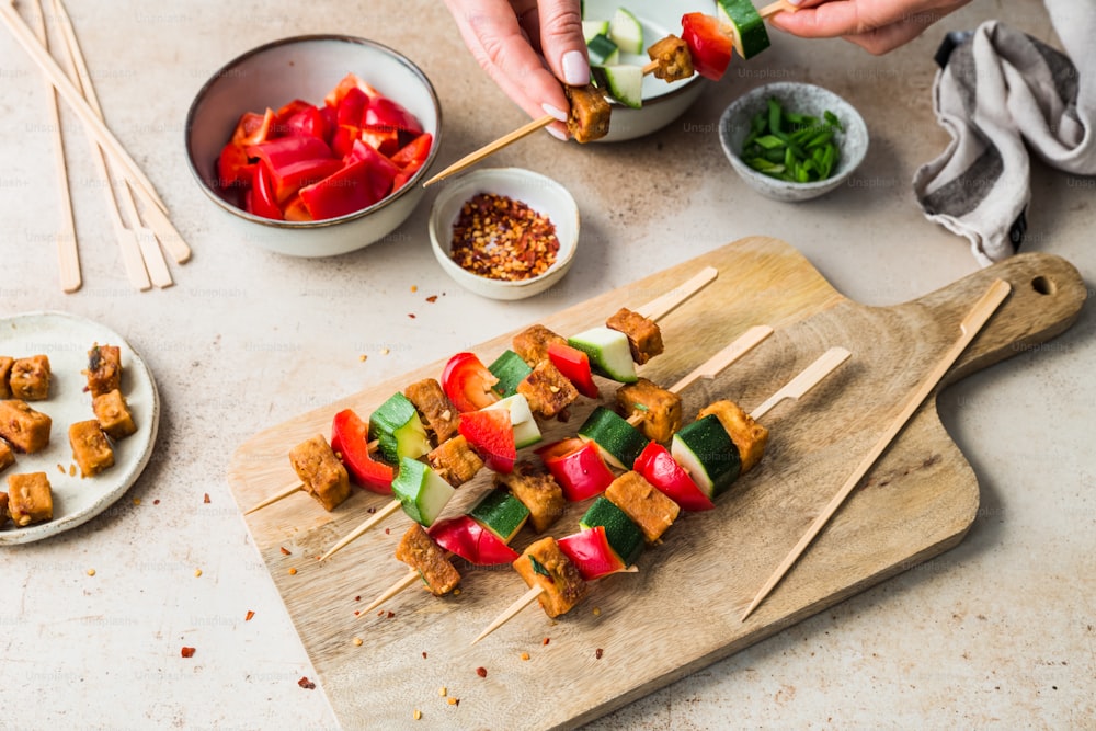 a person holding a skewer of food on a cutting board