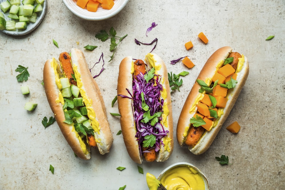 three hot dogs on buns with veggies and mustard