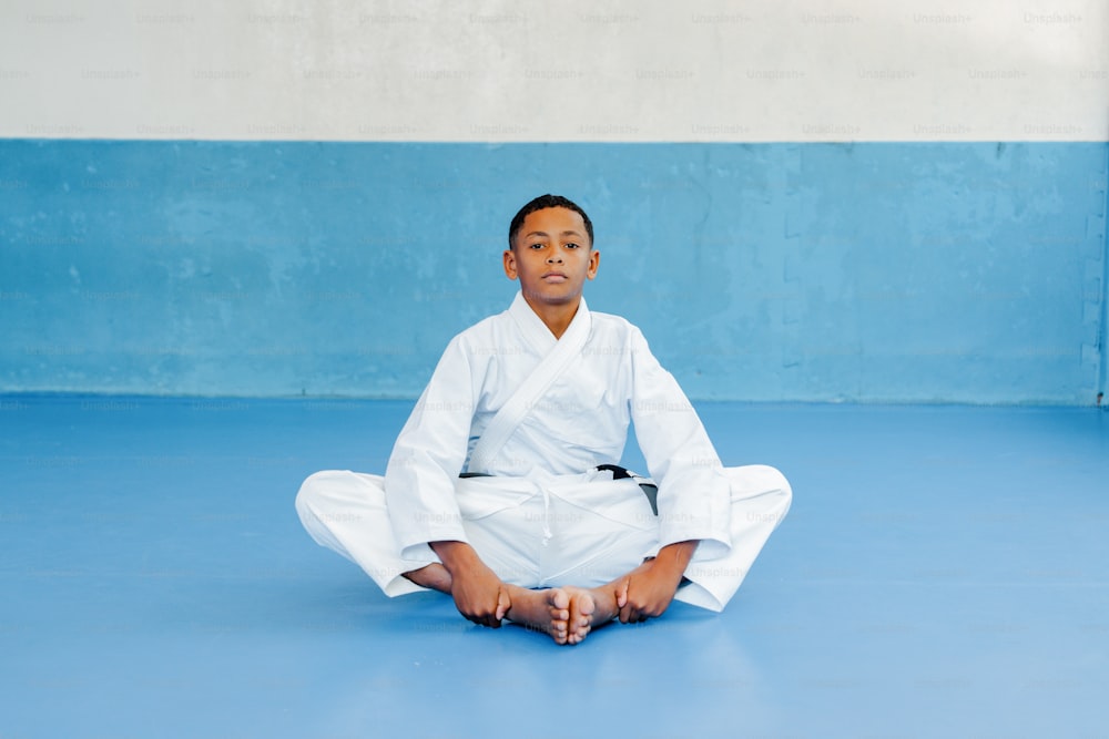 a young boy sitting on a blue floor in a white outfit