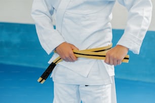 eine Person in weißer Uniform, die einen gelben Gürtel hält