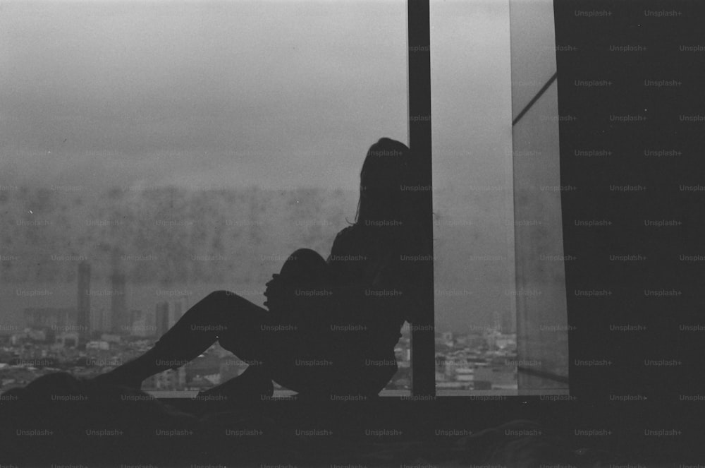 a woman sitting on a window sill looking out at a city