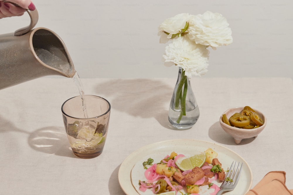 una mesa blanca cubierta con un plato de comida y un jarrón lleno de flores
