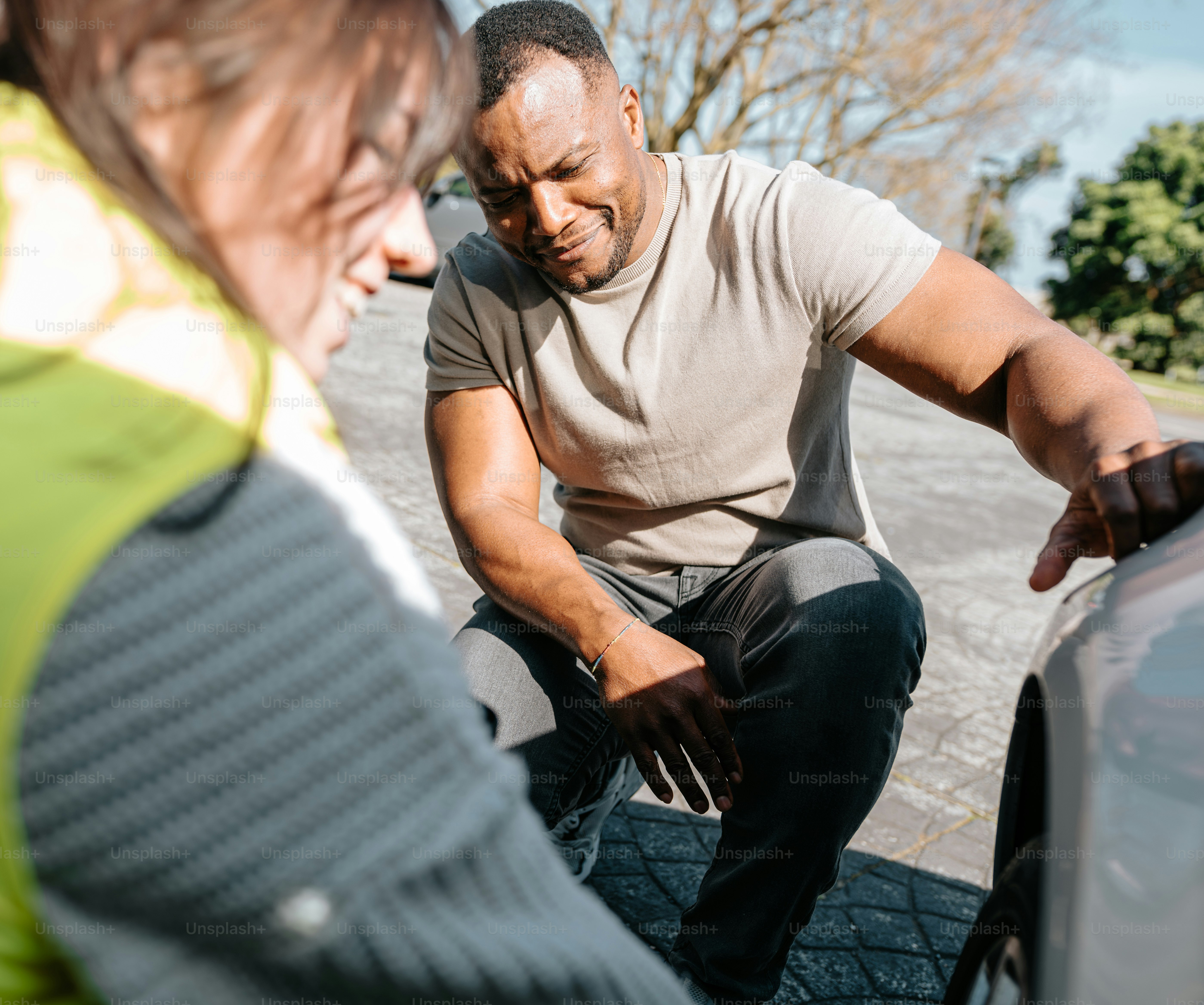 Un hombre sentado en el capó de un coche hablando con una mujer