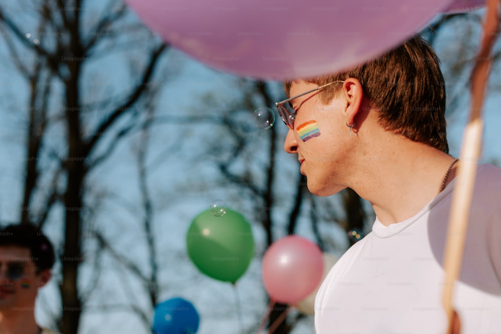 a man with a rainbow painted face standing in front of balloons