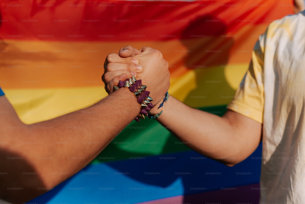 a couple of people holding hands in front of a rainbow flag