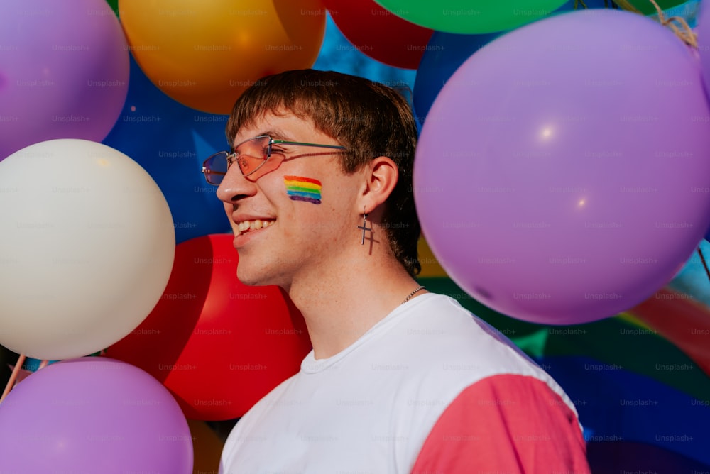 a man with a rainbow painted on his face standing in front of balloons