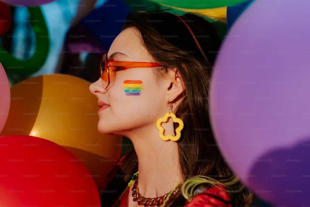 a woman with rainbow painted on her face standing in front of balloons