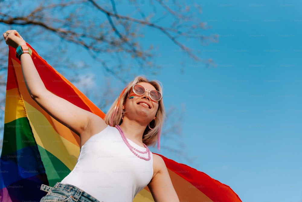 una donna che tiene una bandiera arcobaleno davanti a un albero