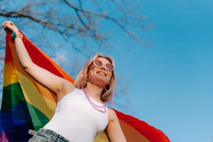 a woman holding a rainbow flag in front of a tree