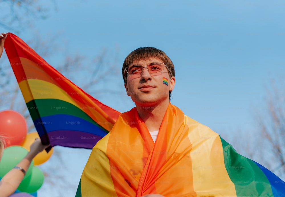 a man holding a rainbow flag and balloons