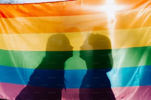 Dos personas sosteniendo una bandera arcoíris frente a un cielo azul