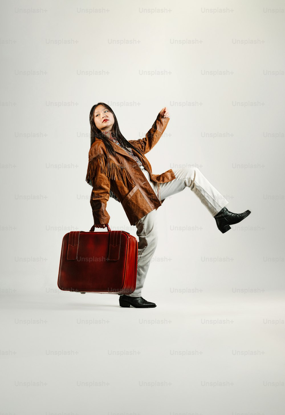 a woman in a brown jacket is holding a red suitcase