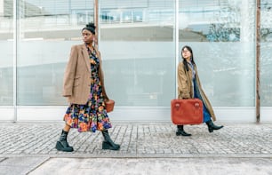 two women walking down a sidewalk with a red suitcase