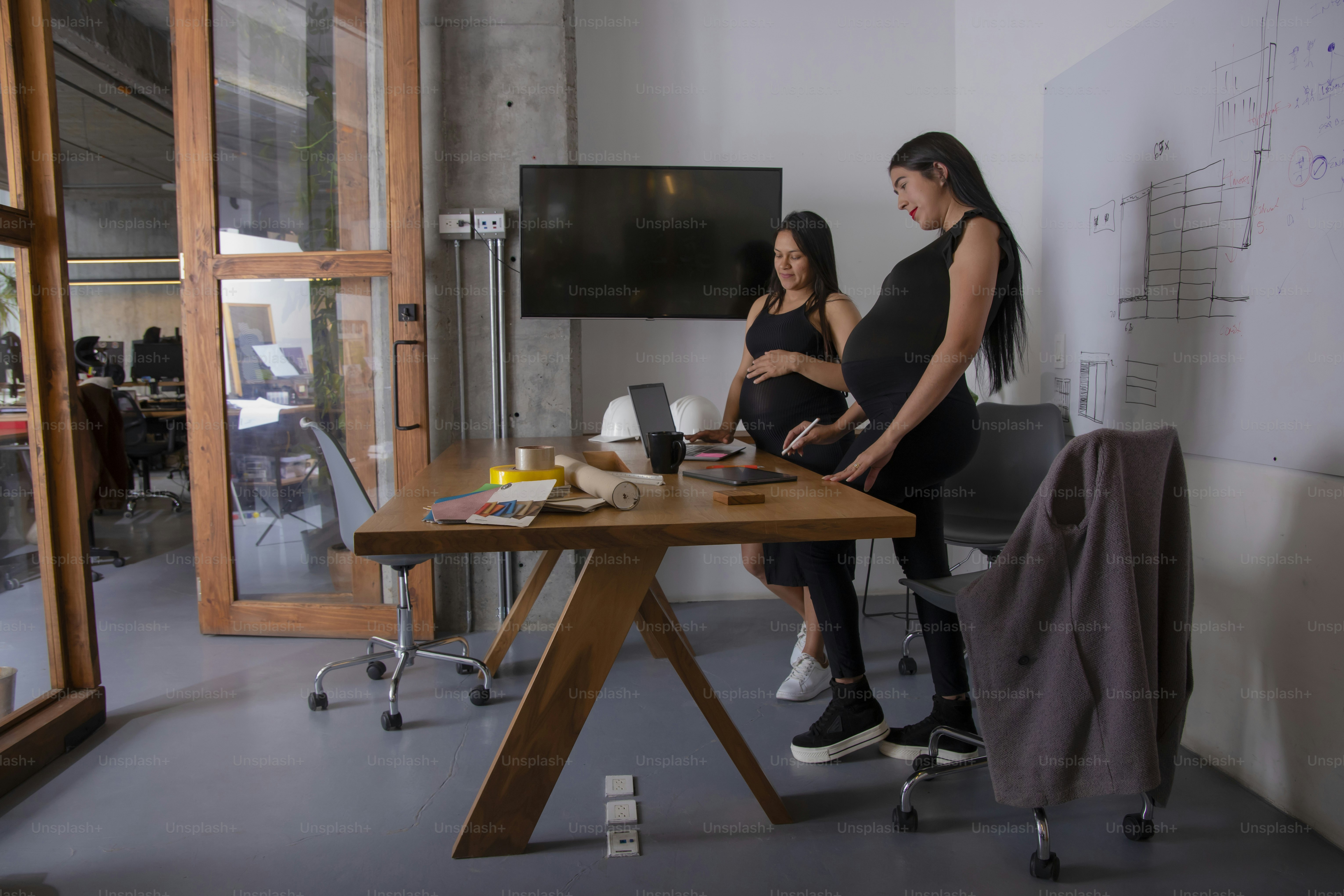 a pregnant woman standing next to a table with a laptop