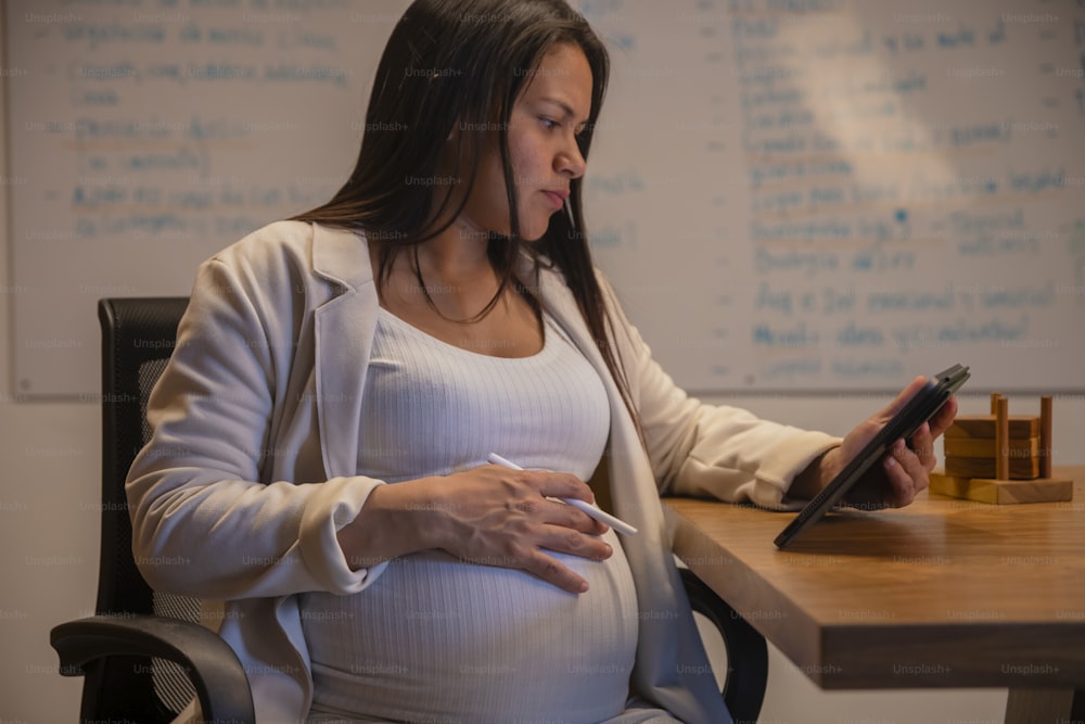 a pregnant woman sitting at a desk using a tablet
