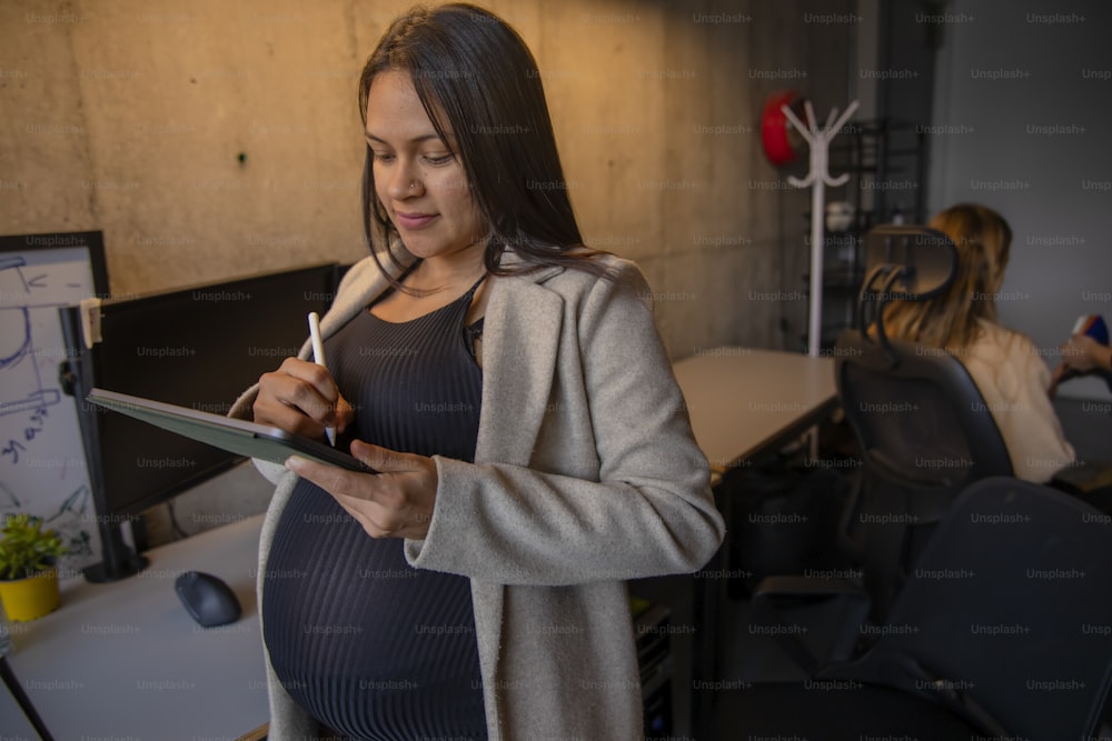eine schwangere Frau, die in einem Büro auf ein Klemmbrett schreibt