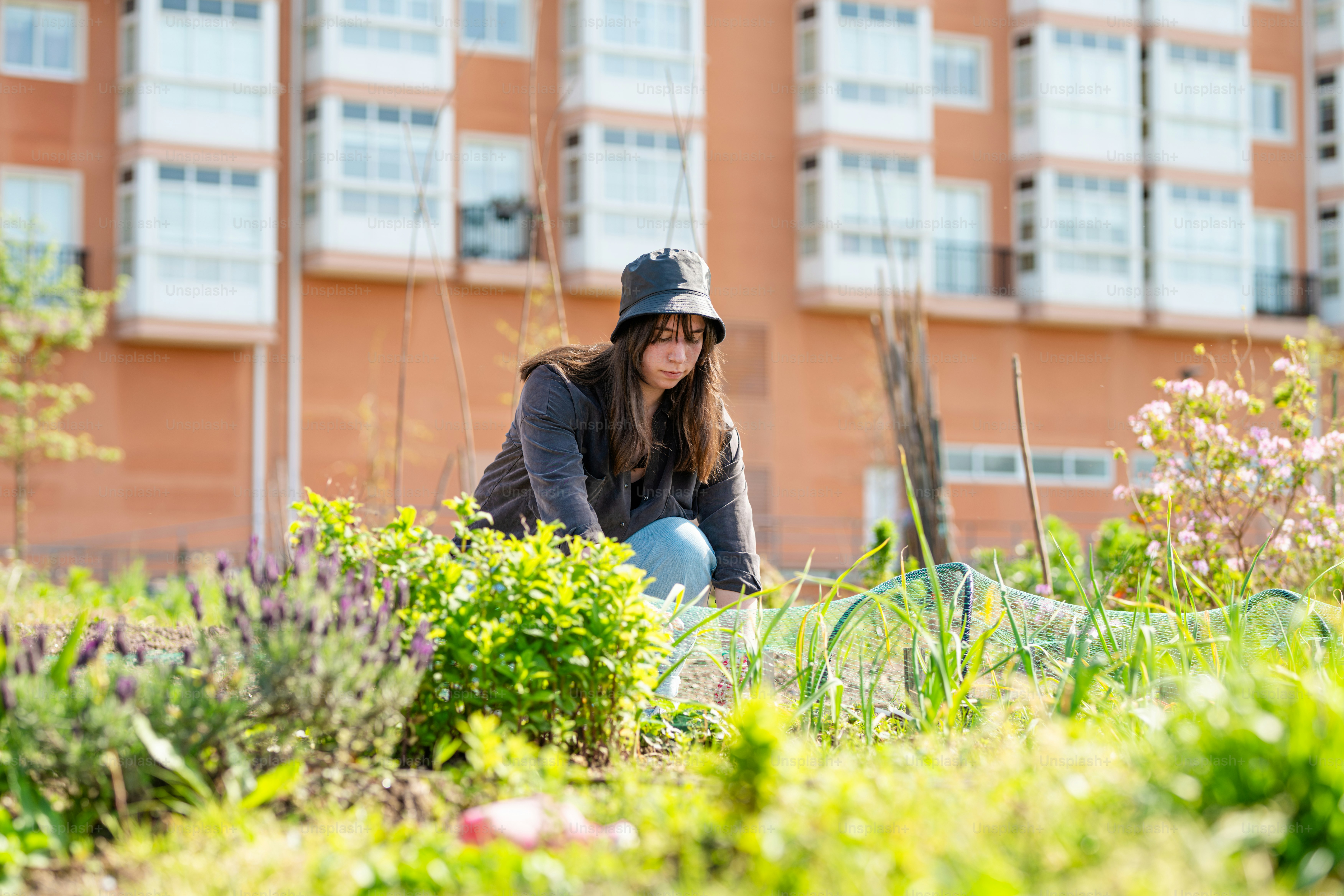 a woman kneeling down in a garden with a building in the background