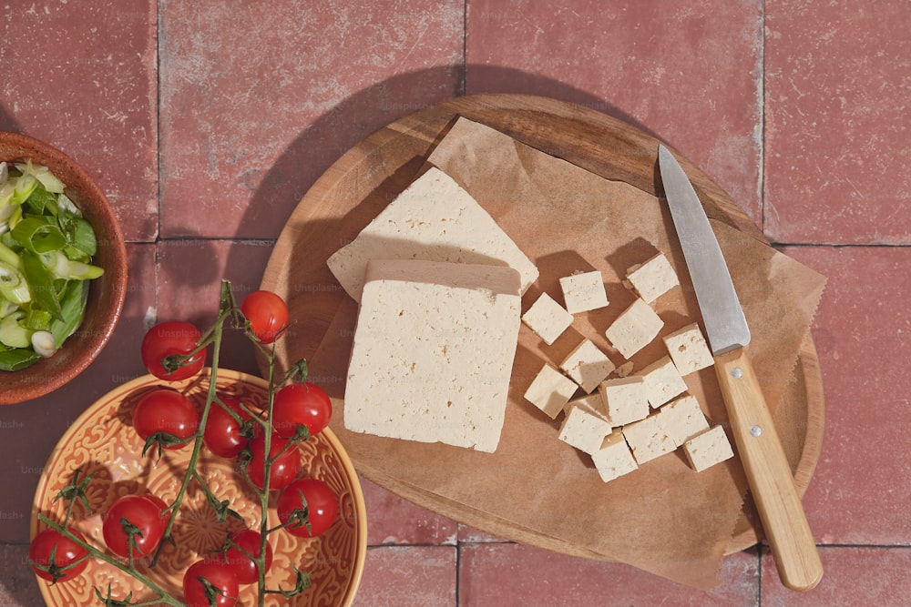 uma tábua de corte coberta com queijo fatiado ao lado de uma tigela de salada