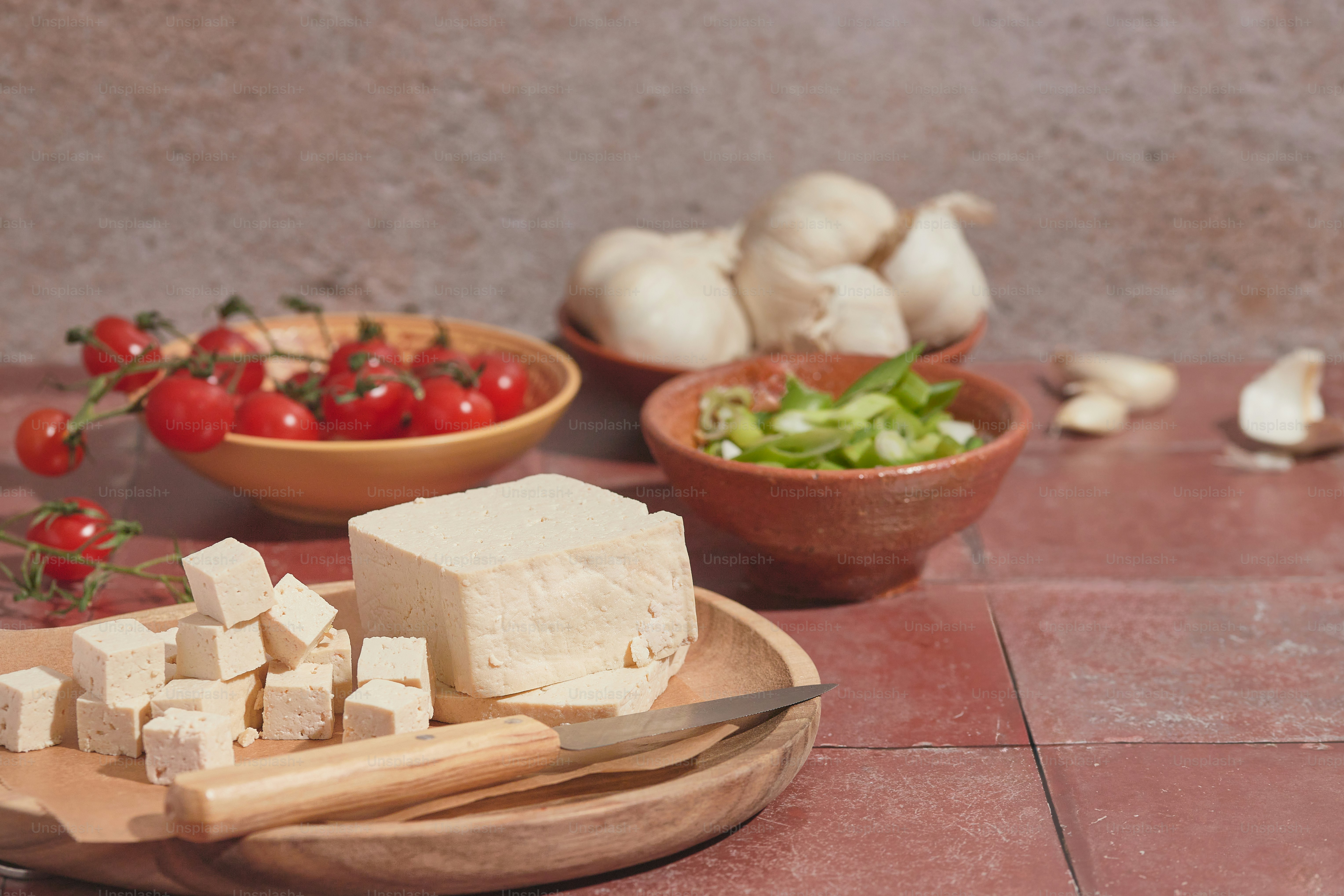 a wooden plate topped with tofu next to bowls of vegetables