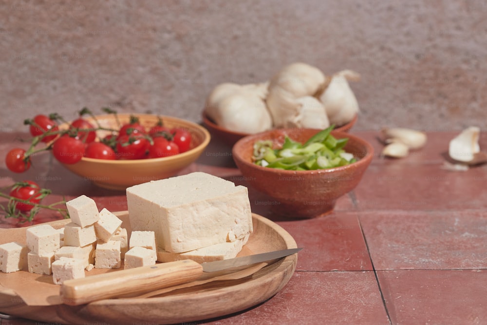 ein Holzteller mit Tofu neben Schüsseln mit Gemüse