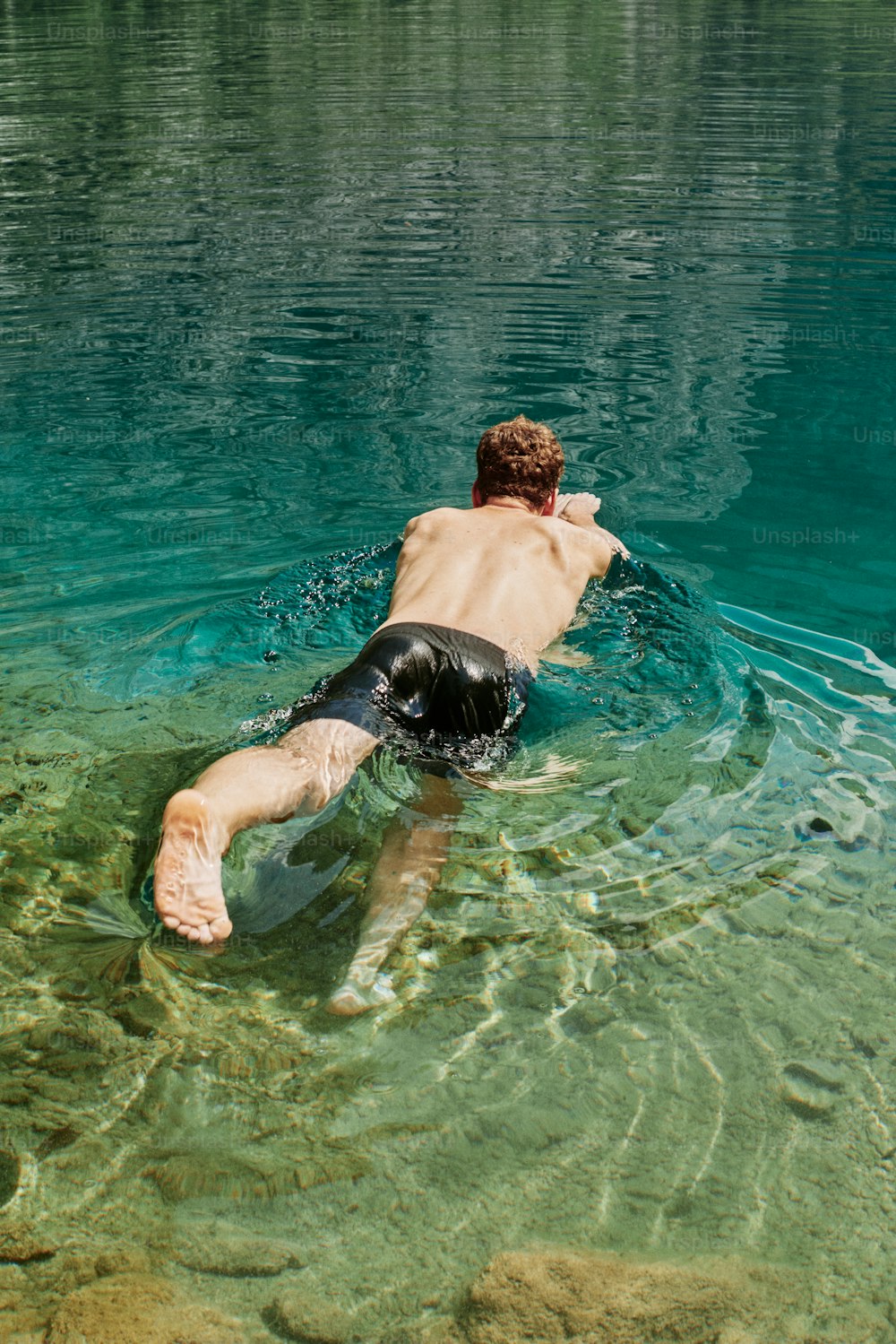 a man swimming in a lake with his back to the camera