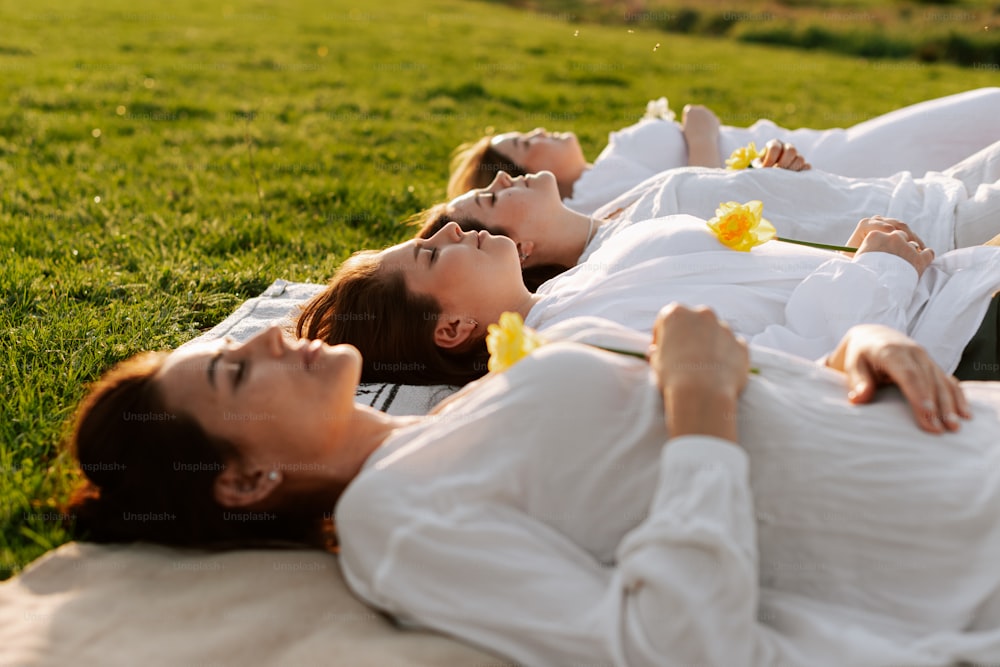 a couple of women laying on top of a lush green field