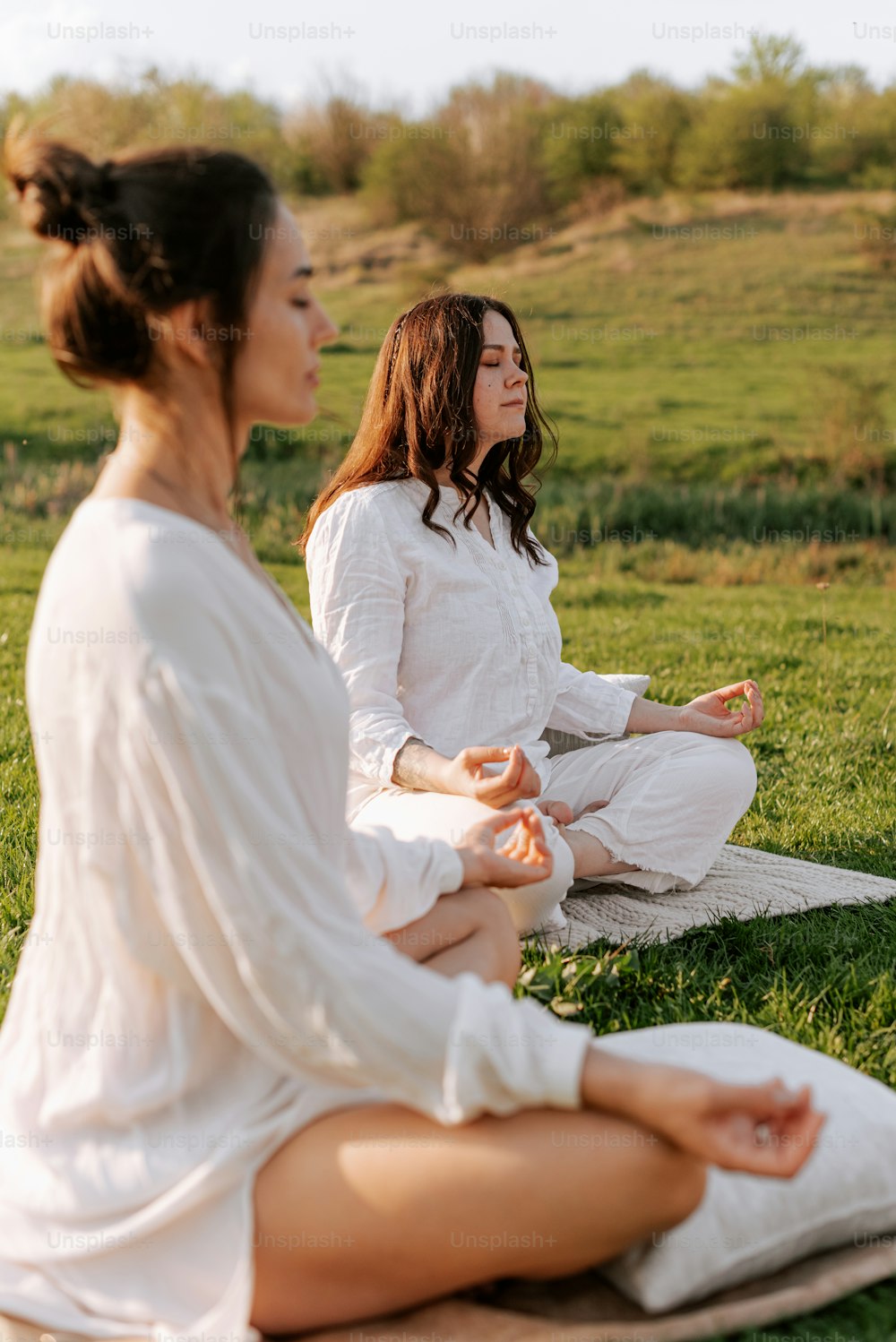 two women sitting in a field doing yoga