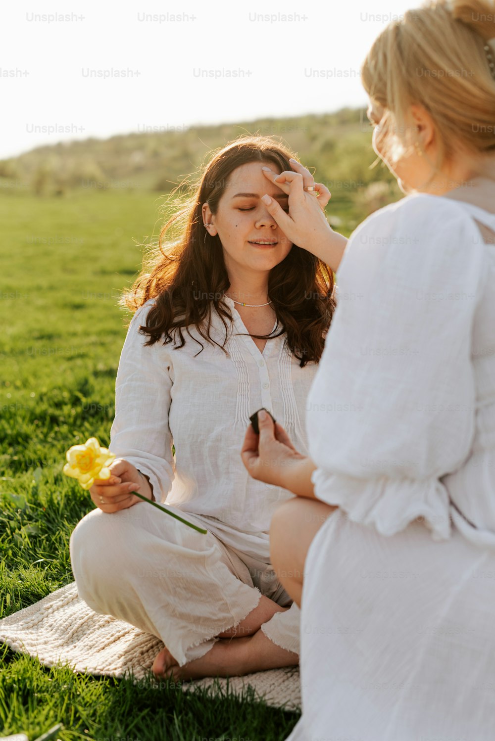 a woman sitting on a blanket holding a flower