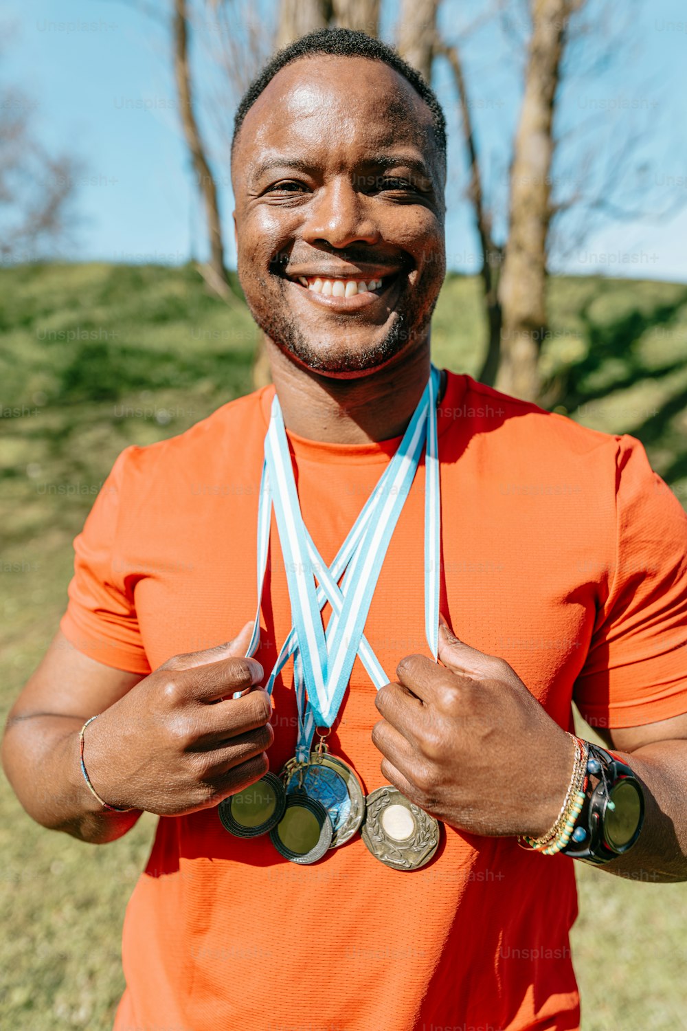 a man in an orange shirt holding two medals