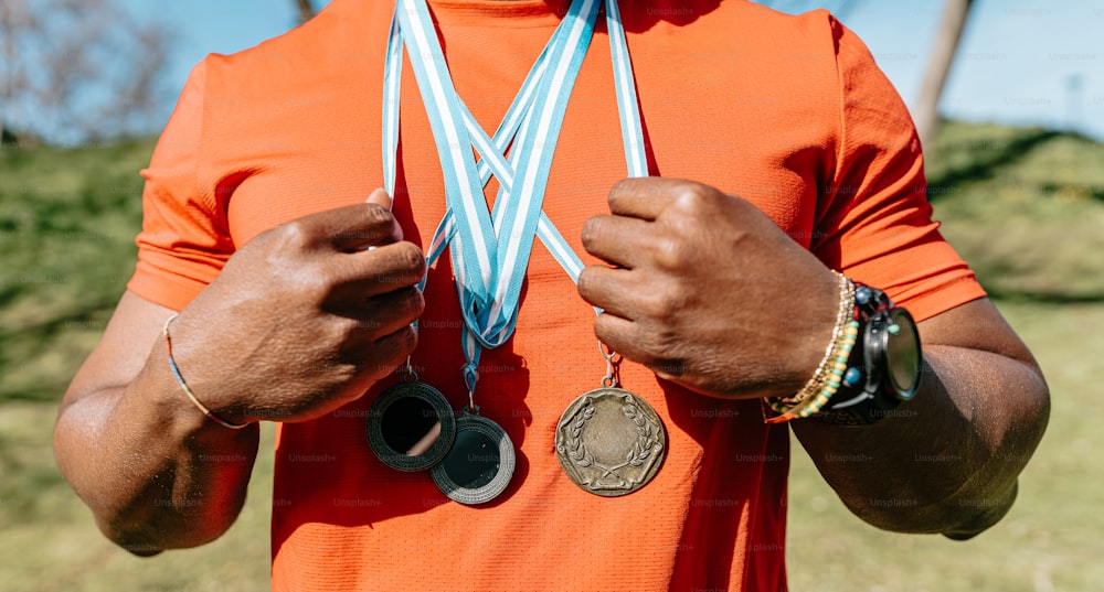 a man in an orange shirt holding two medals