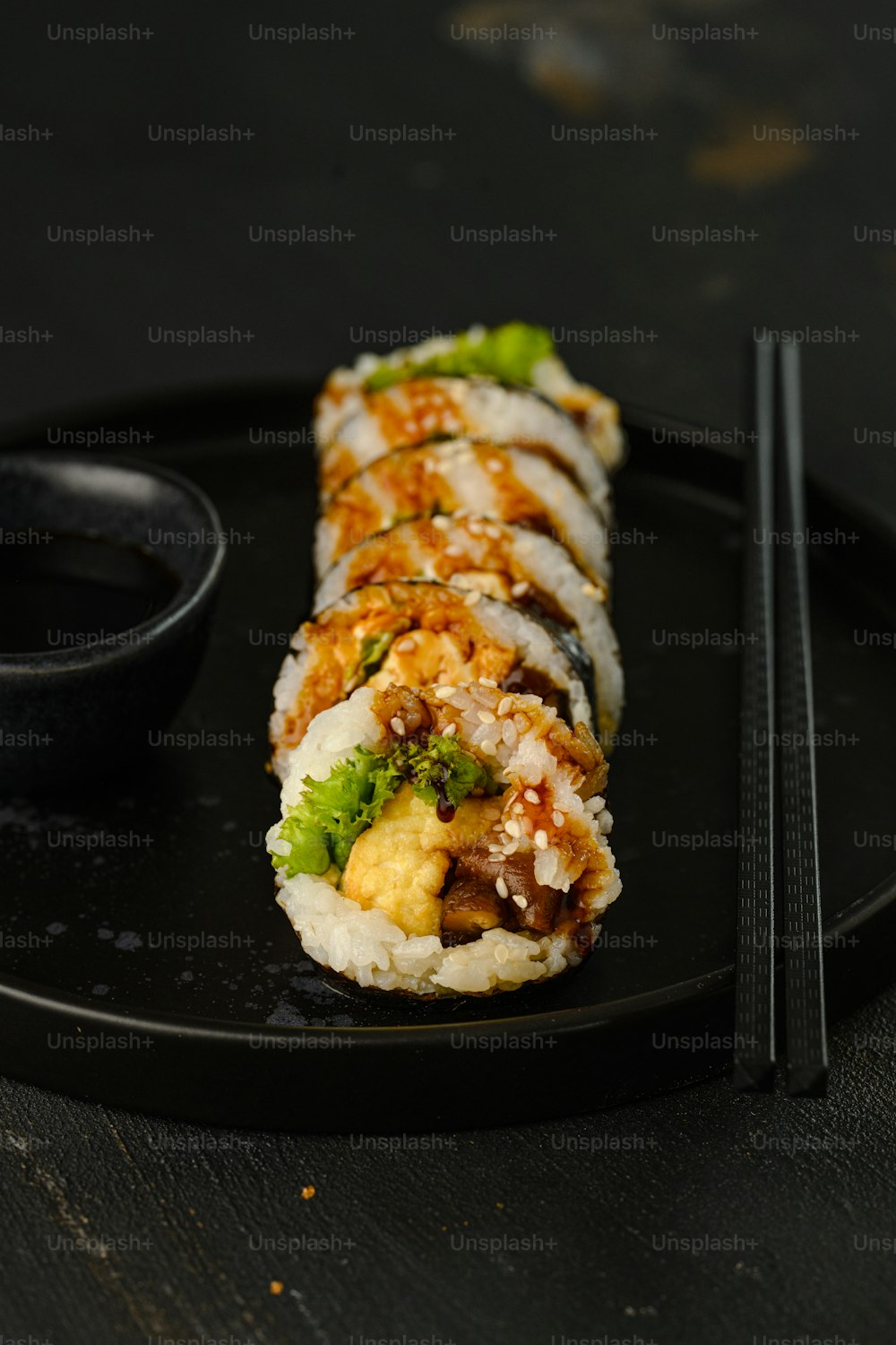 um prato preto coberto com sushi e pauzinhos