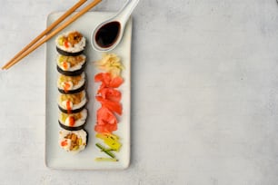 un plato blanco cubierto con sushi y palillos