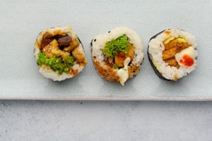 três rolos de sushi em um prato branco sobre uma mesa