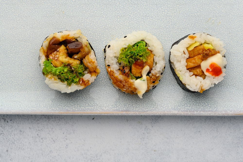 Tres rollos de sushi en un plato blanco sobre una mesa