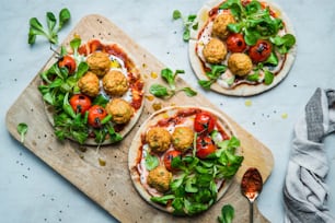 two pizzas with meatballs and vegetables on a cutting board