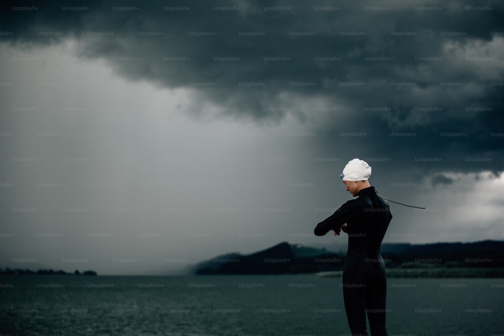 a man in a wet suit standing on a beach under a cloudy sky