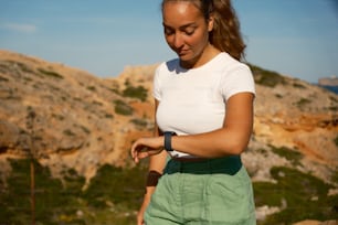 Una mujer con camisa blanca y pantalones cortos verdes sosteniendo un teléfono celular