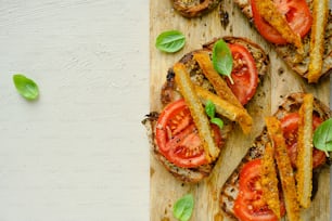 a wooden cutting board topped with sandwiches covered in tomatoes