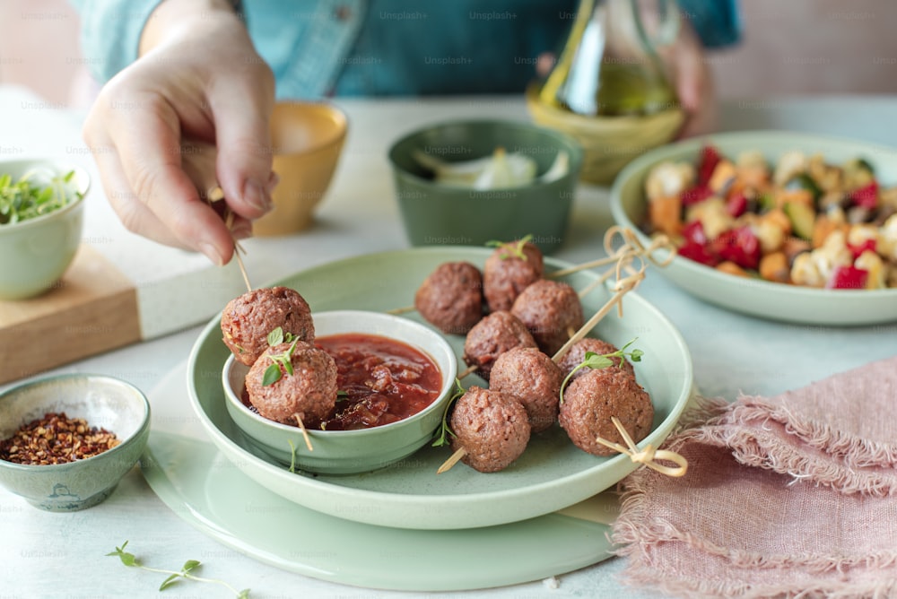 a person dipping sauce into a bowl of meatballs