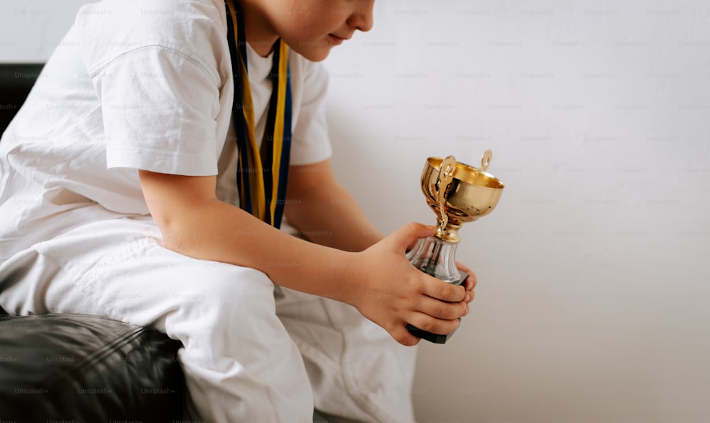a young boy sitting on a chair holding a trophy