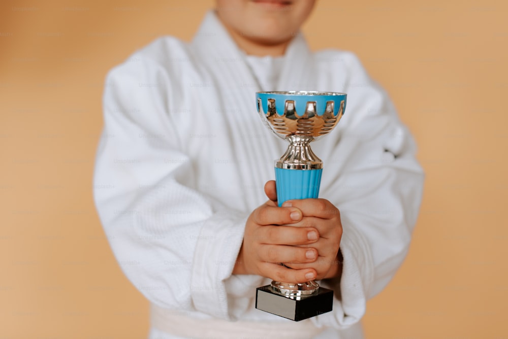 a young boy holding a blue and silver trophy