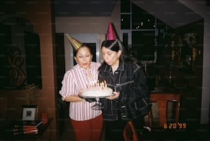 Un par de mujeres de pie una al lado de la otra sosteniendo un pastel