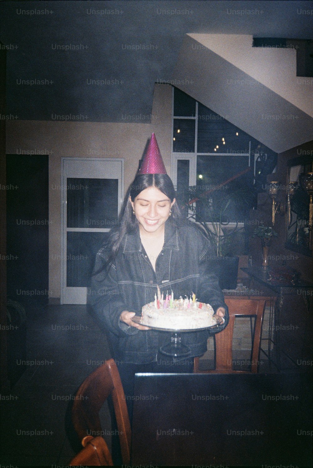 eine Frau mit Partyhut hält eine Geburtstagstorte in der Hand