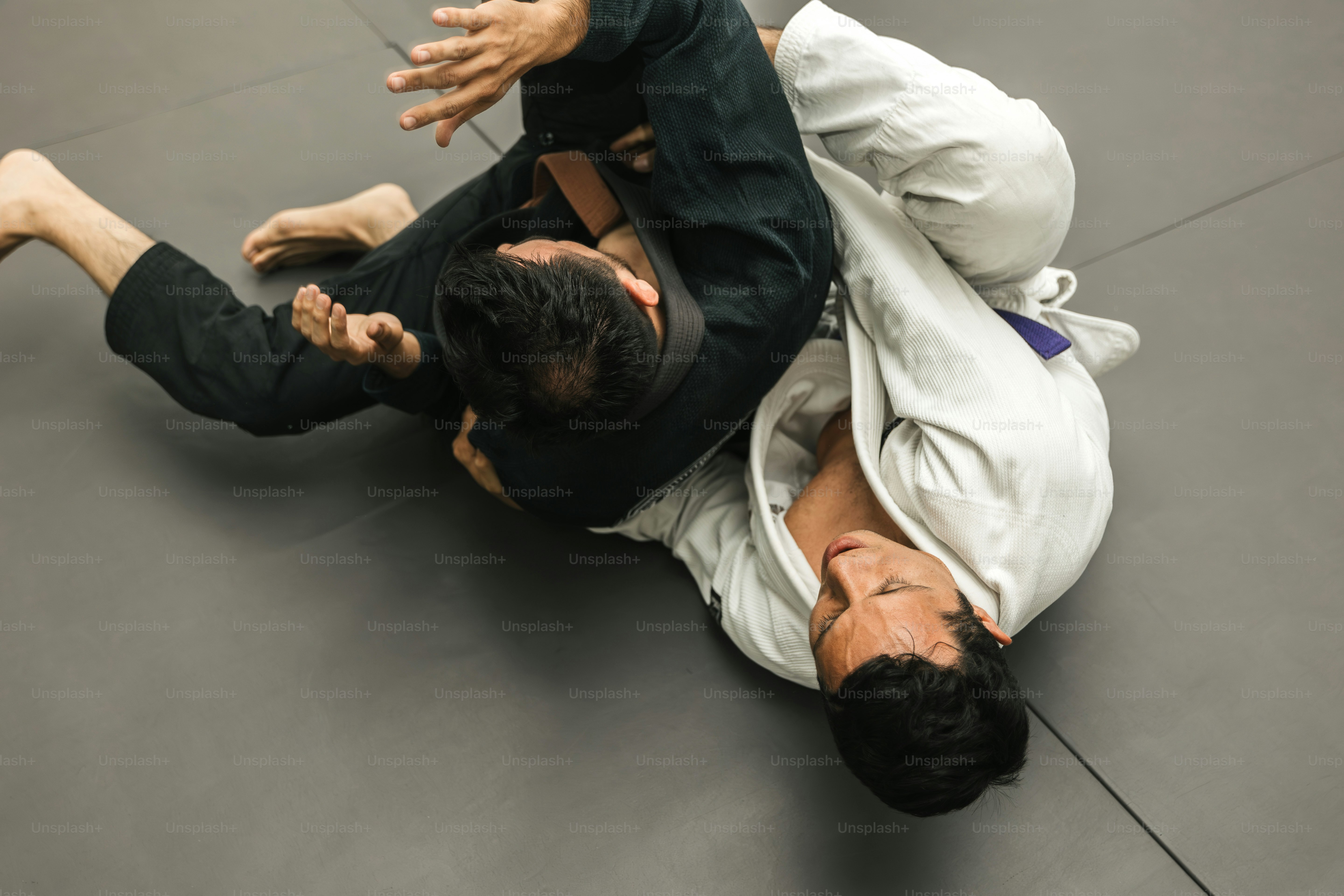 Un hombre con camisa negra y pantalones blancos sobre una colchoneta negra